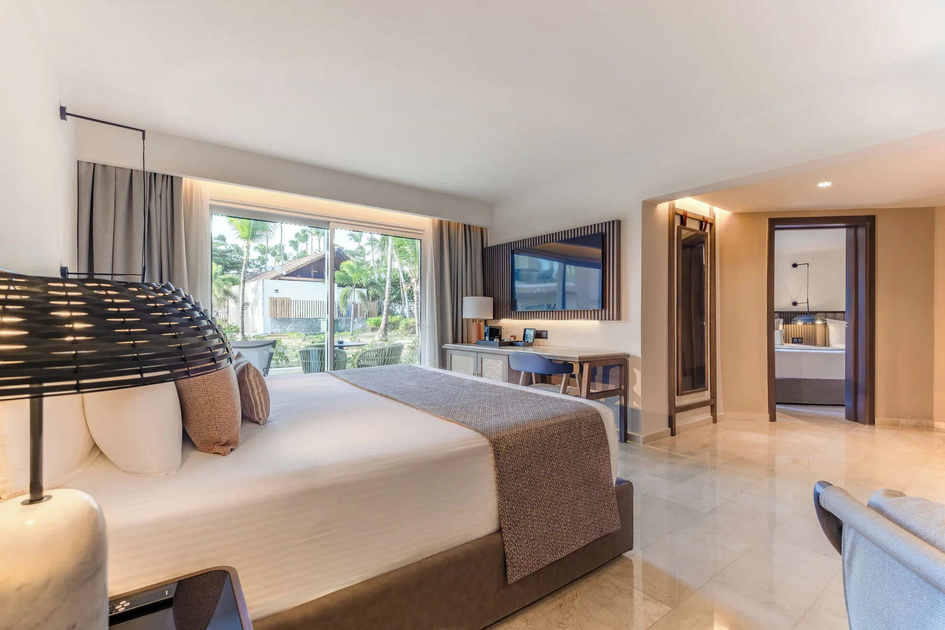 Spacious king bed guest room with TV, desk, and balcony at Grand Palladium Select Bávaro.