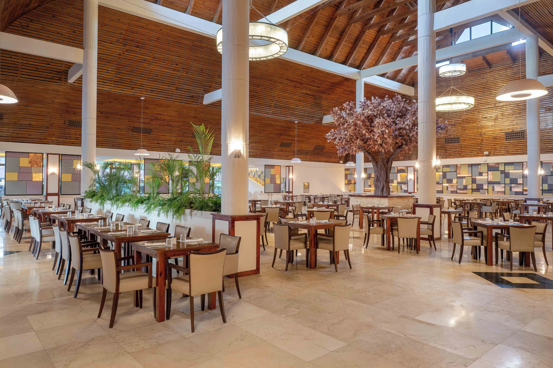 Large dining room with wood ceiling and set tables at Grand Palladium Select Bávaro.