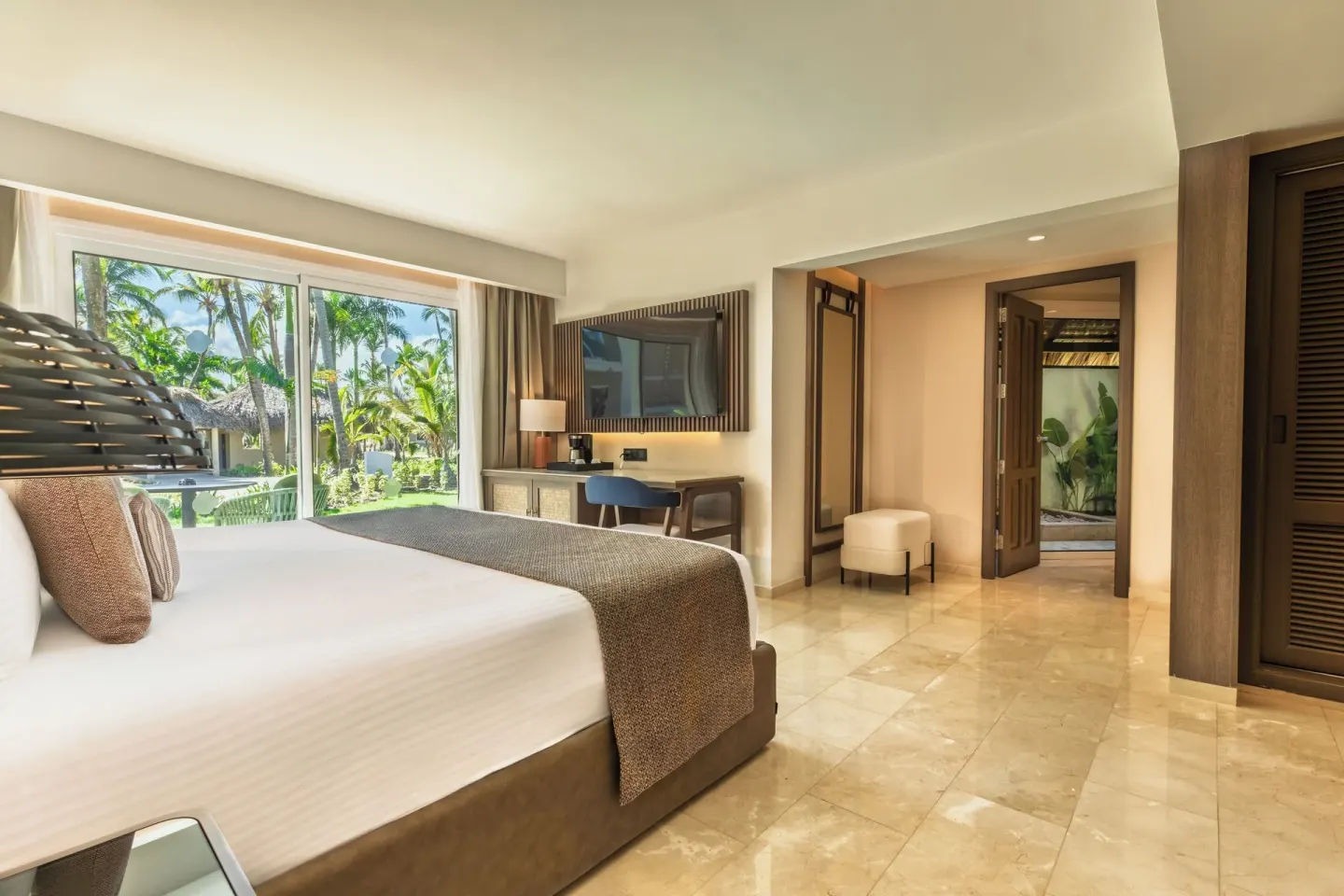 Romance Suite Garden View king bed, TV, desk, and garden doors at Grand Palladium Select Bávaro.