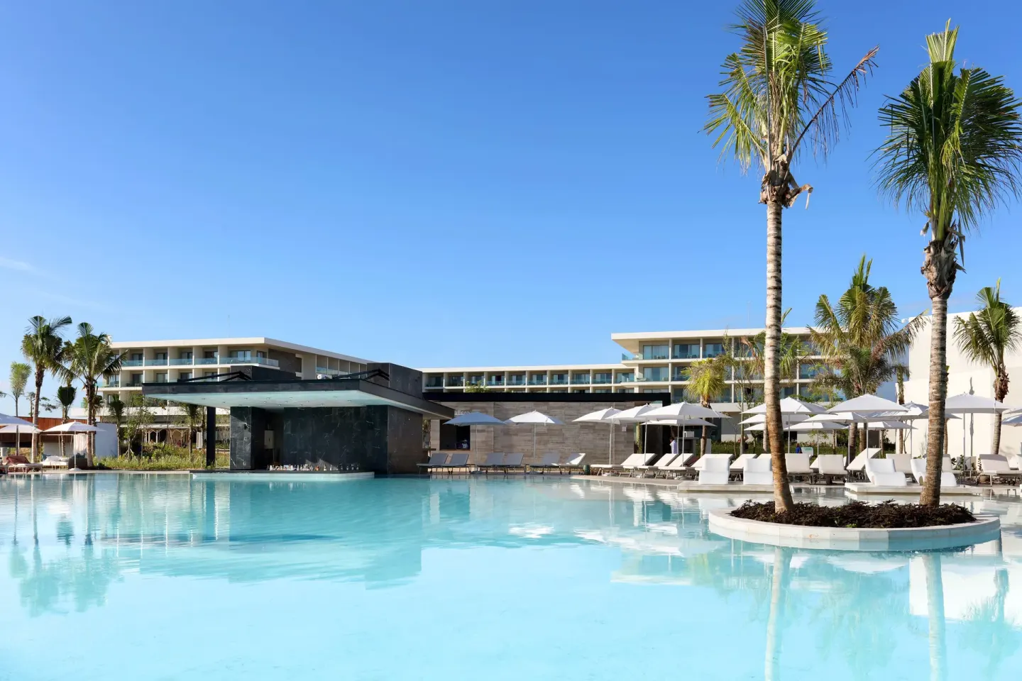 Resort pool with palm island and guest buildings at Grand Palladium Select Costa Mujeres.