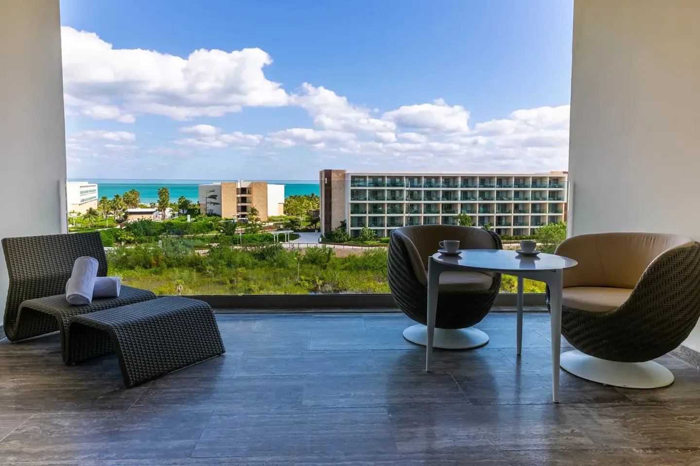 Junior Suite Ocean View balcony with chairs, table, and distant sea at Grand Palladium Select Costa Mujeres.