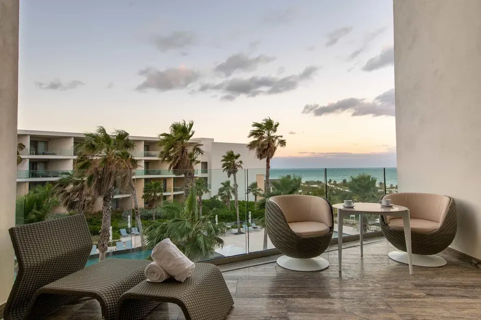 Junior Suite Ocean View terrace with seating and sunset sea view at Grand Palladium Select Costa Mujeres.
