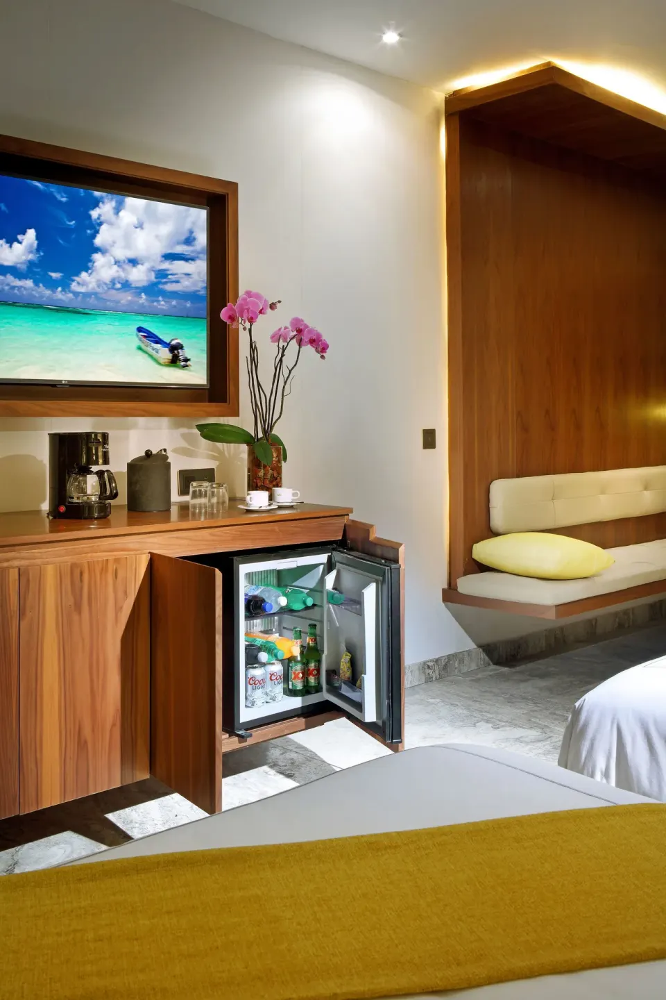 Junior Suite refreshment area with TV, open minibar, and bench at Grand Palladium Select Costa Mujeres.