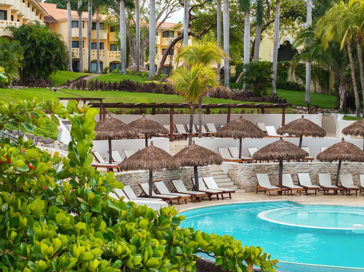 Pool loungers under thatched umbrellas at Grand Palladium Vallarta Resort & Spa.