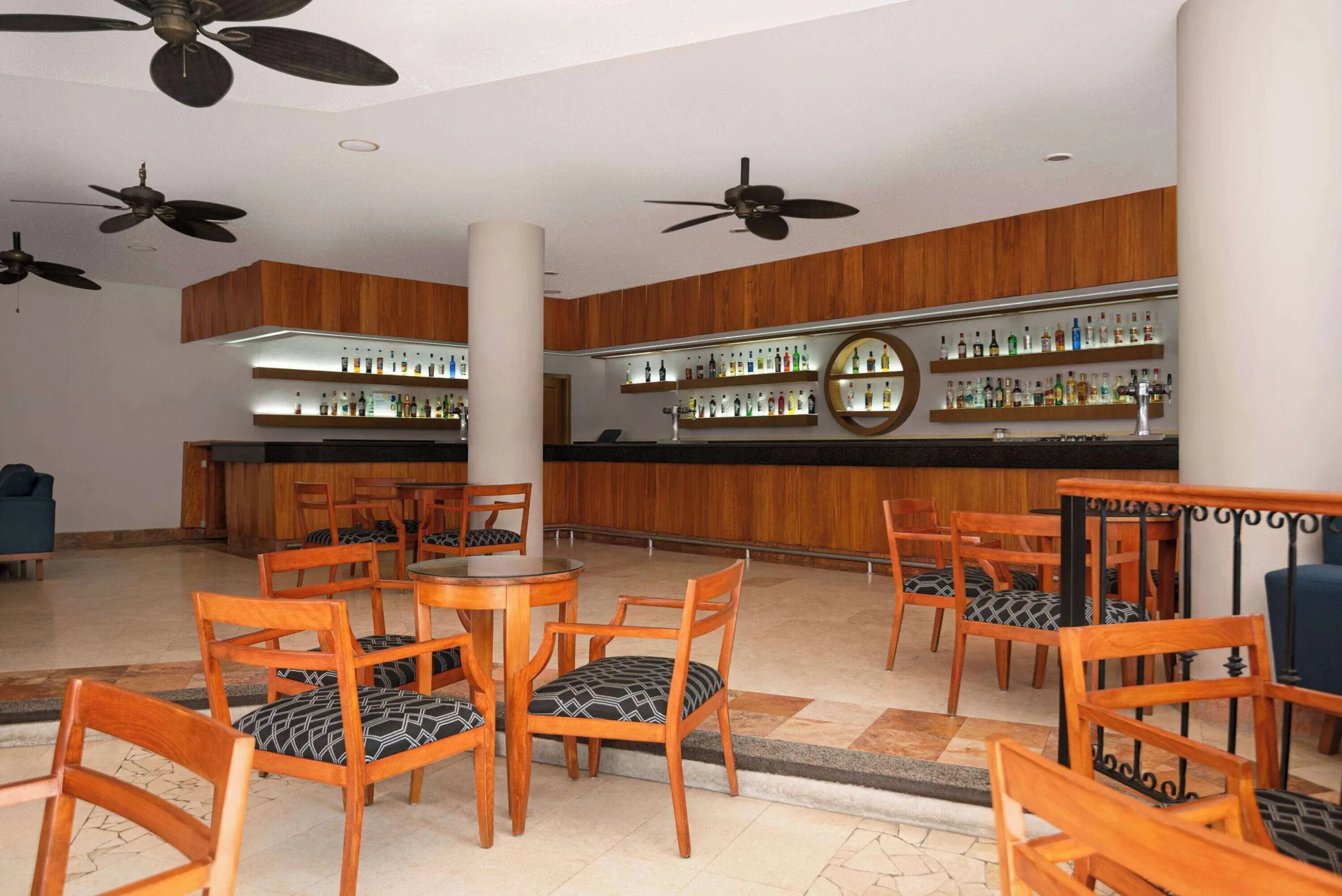 Lobby bar with wood tables and backlit shelves at Grand Palladium Vallarta Resort & Spa.