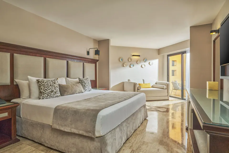 Junior Suite king bed with sofa and balcony doors at Grand Palladium Vallarta Resort & Spa.