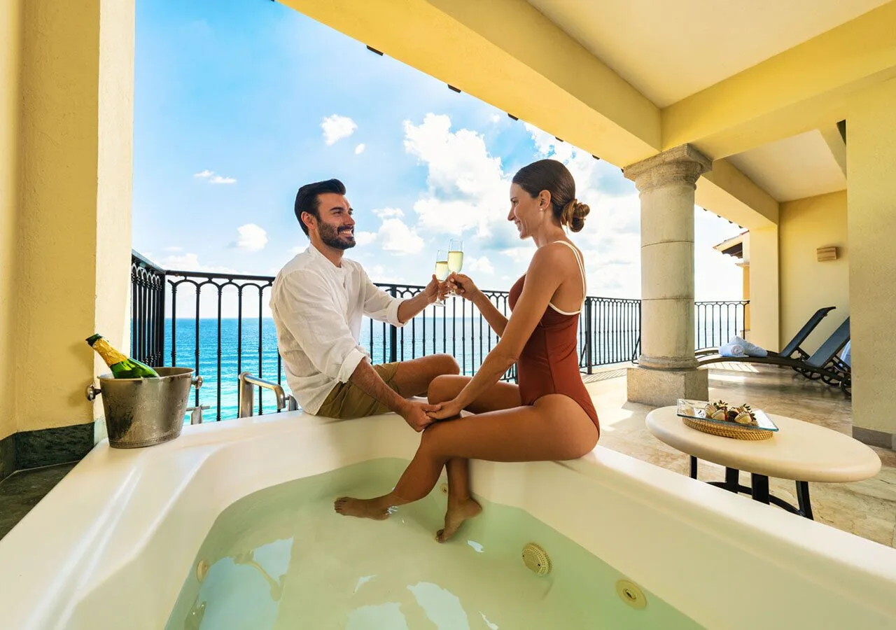 Couple toasting in a balcony whirlpool with ocean view at Grand Park Royal Cancun.