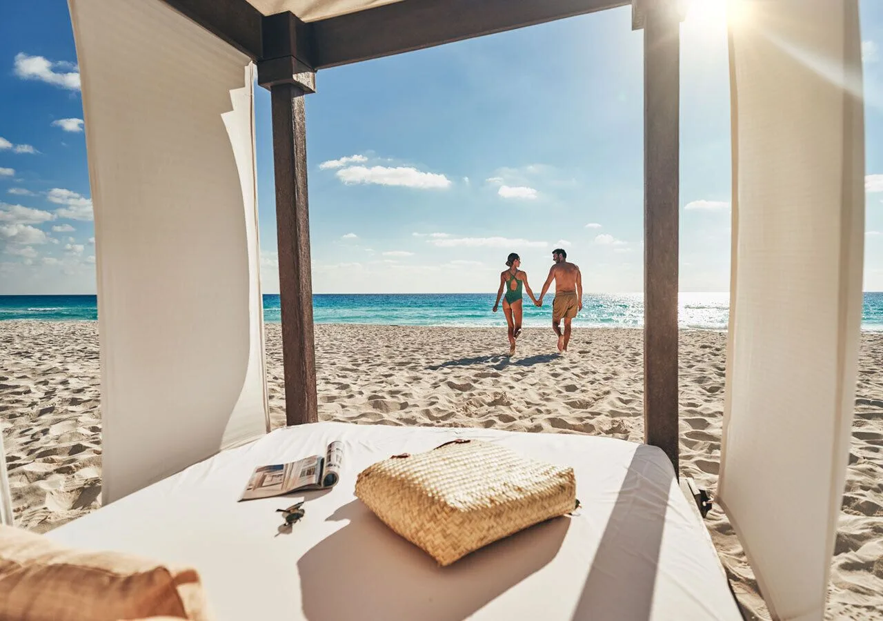 Beach cabana bed frames guests walking toward the ocean at Grand Park Royal Cancun.