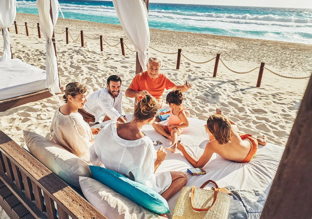 Family gathered on a shaded beach daybed at Grand Park Royal Cancun.