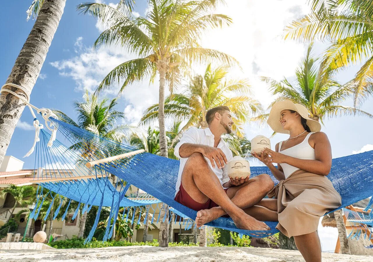 Guests relax in a blue beach hammock beneath palms at Grand Park Royal Cancun.