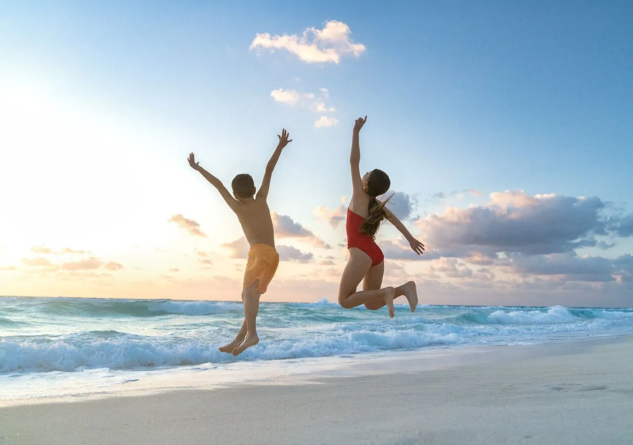 Two children jump on the beach near the waves at Grand Park Royal Cancun.