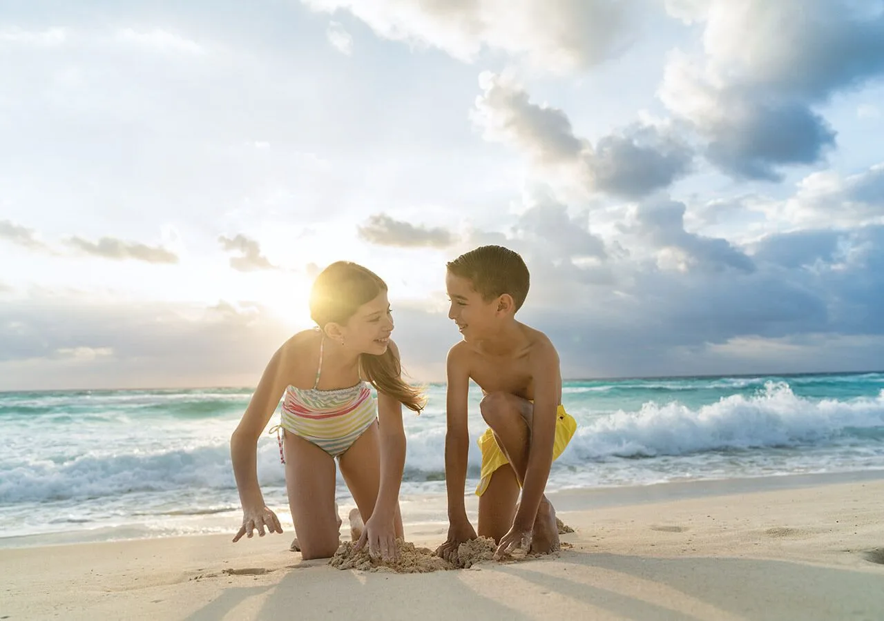 Children kneel in the sand near breaking waves at Grand Park Royal Cancun.