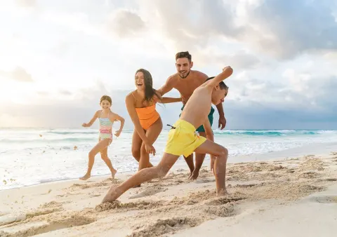 Family running and laughing on the beach at Grand Park Royal Cancun.