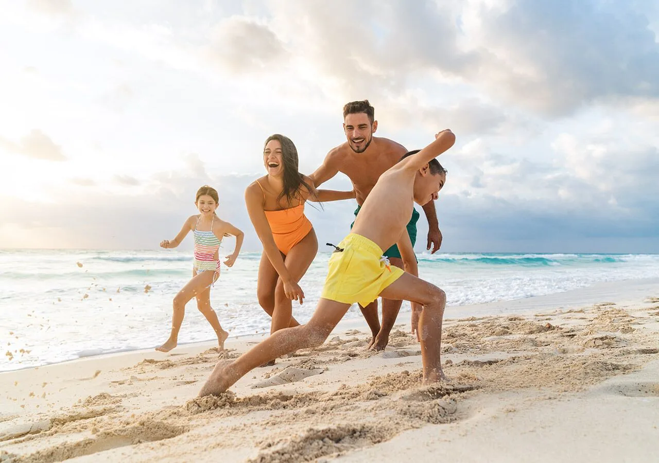 Family running and laughing on the beach at Grand Park Royal Cancun.