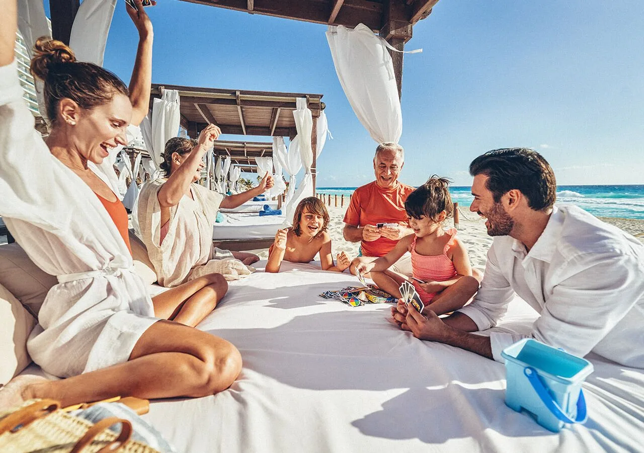 Family plays cards on a shaded beach cabana at Grand Park Royal Cancun.