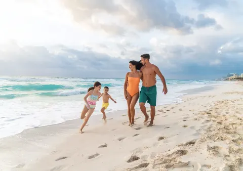 Family walking along the shoreline by the waves at Grand Park Royal Cancun.
