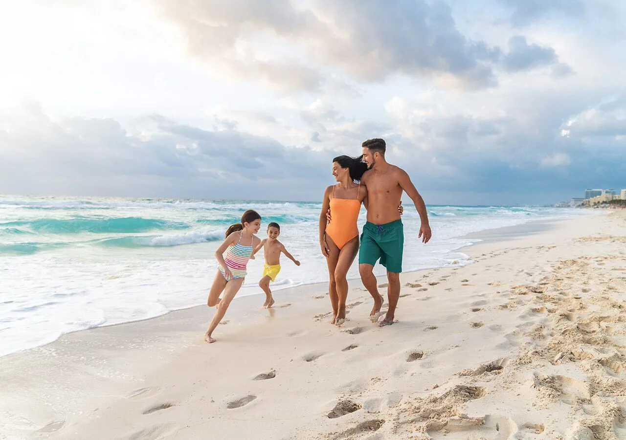Family walking along the shoreline by the waves at Grand Park Royal Cancun.