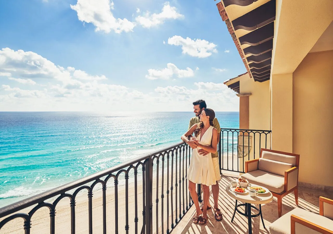 Couple on an oceanfront balcony at Grand Park Royal Cancun overlooking the turquoise sea.