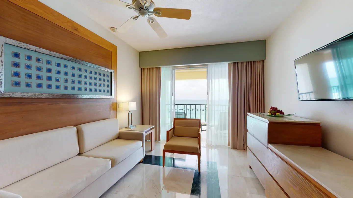 Master Suite living room with sofa, TV and balcony doors at Grand Park Royal Cancun.