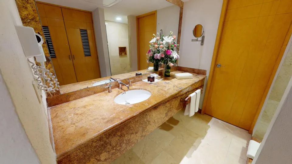 Long marble vanity with sink and floral arrangement in a Grand Park Royal Cozumel bathroom.