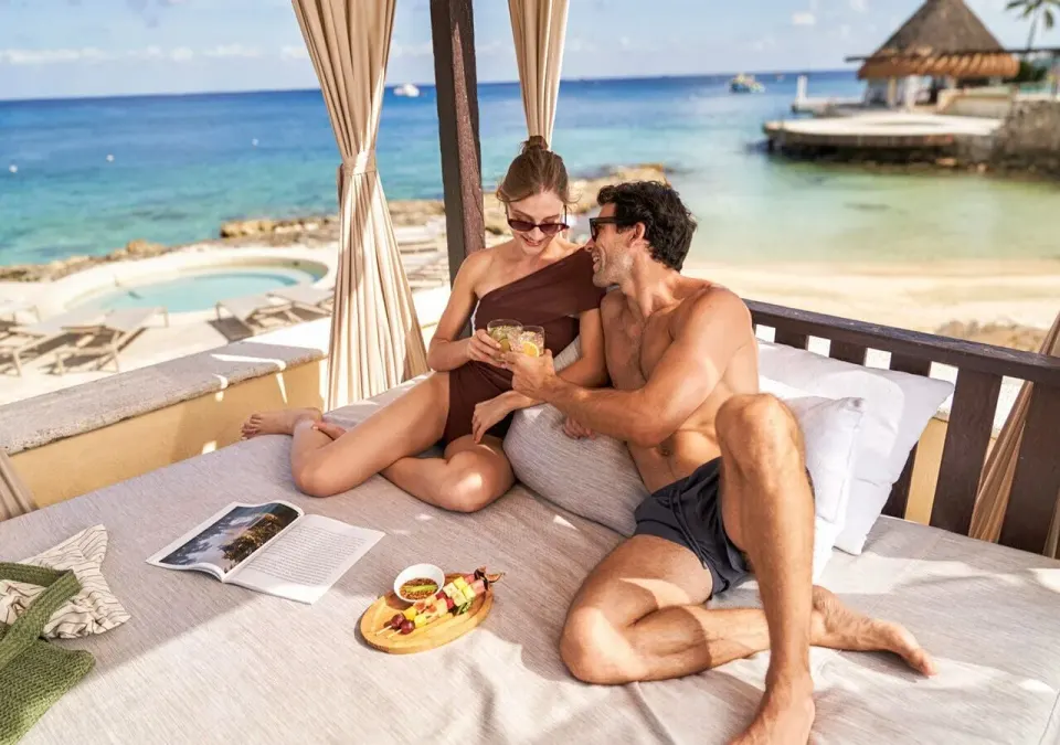 Couple sharing drinks and snacks in a shaded cabana by the beach at Grand Park Royal Cozumel.