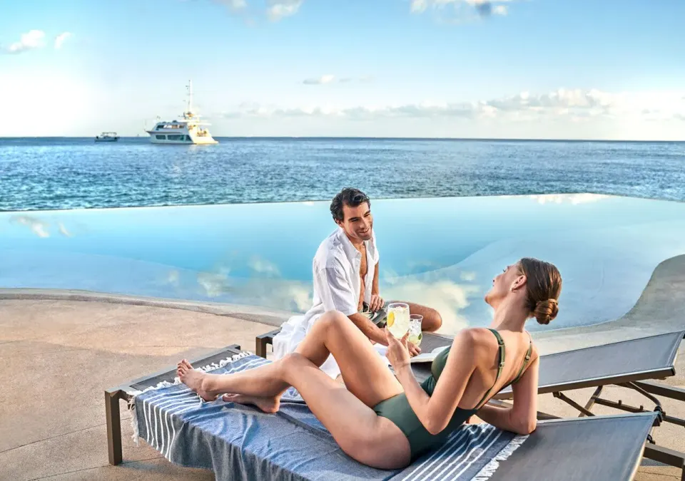 Couple relaxing on loungers beside an infinity pool overlooking the sea at Grand Park Royal Cozumel.