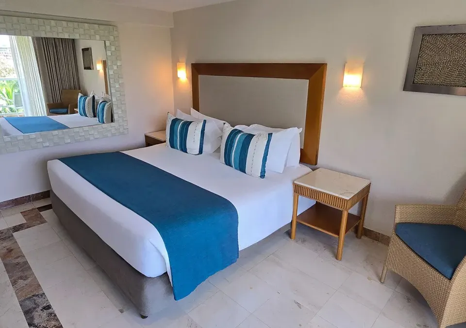 King bed with large decorative mirror and wicker chair in a Grand Park Royal Cozumel room