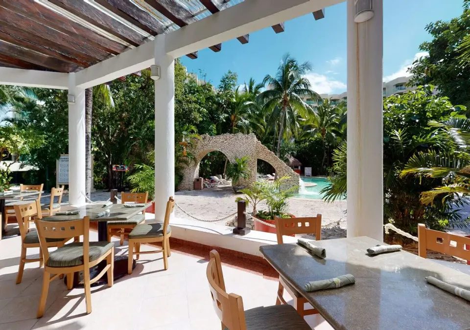Shaded poolside dining terrace with tables overlooking tropical pool at Grand Park Royal Cozumel