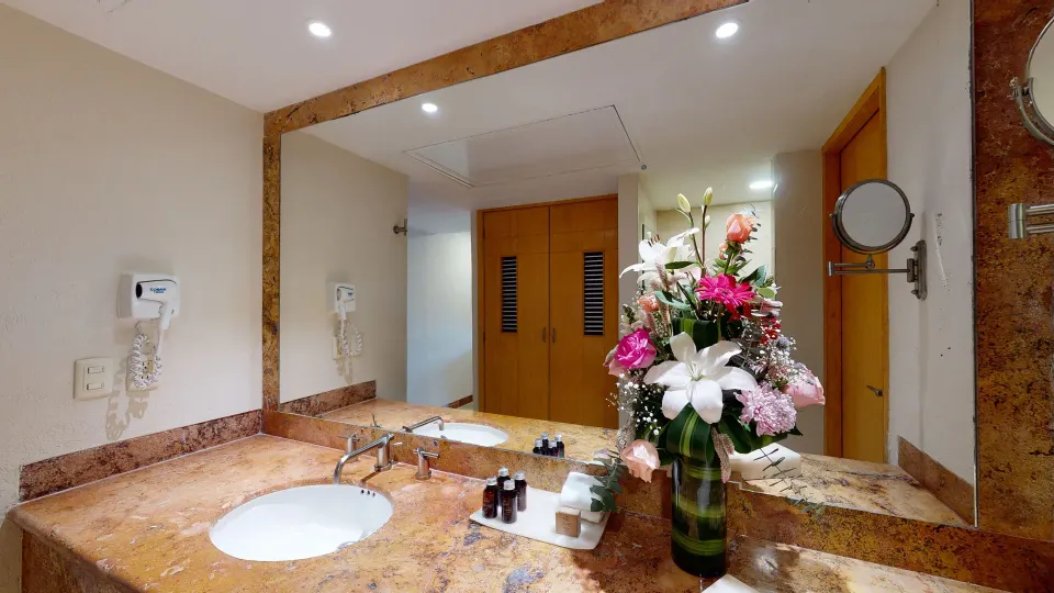 Marble sink, mirror and floral arrangement in a guest bathroom at Grand Park Royal Cozumel.
