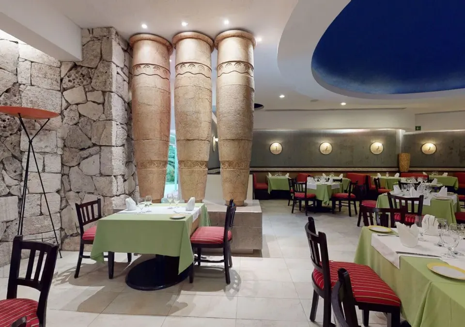 Elegant indoor restaurant with stone columns and green tablecloths at Grand Park Royal Cozumel