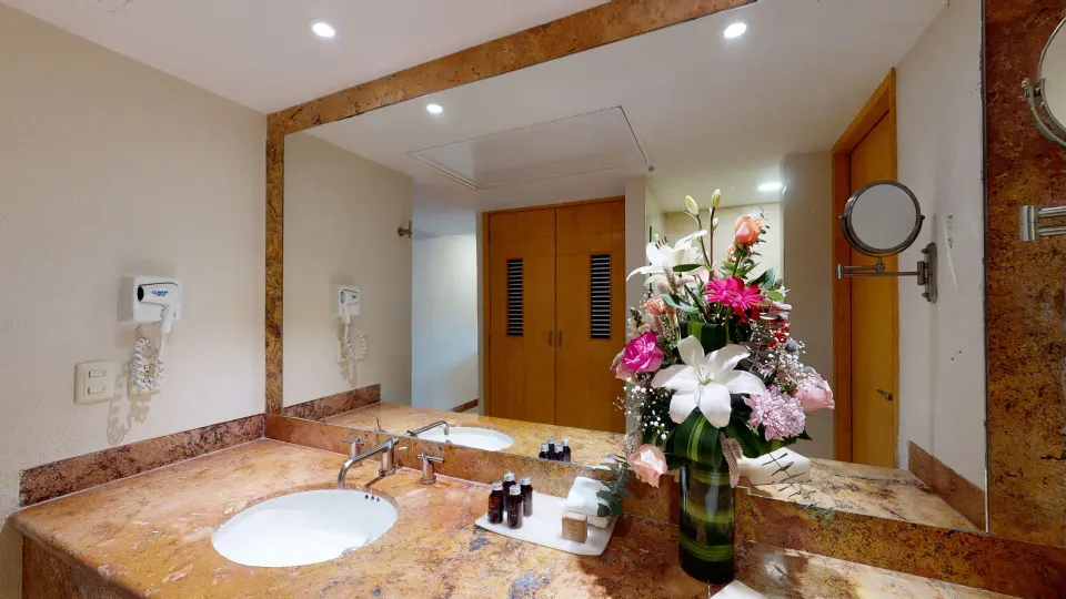 Bathroom vanity with mirror and floral arrangement in a deluxe room at Grand Park Royal Cozumel