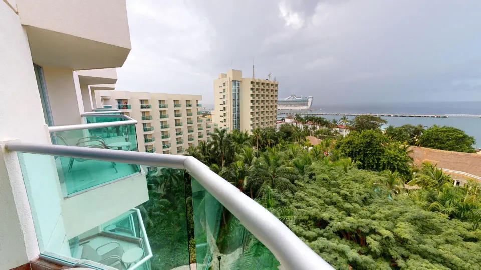 Balcony view over palms and hotel grounds toward the sea and a distant cruise ship at Grand Park Royal Cozumel