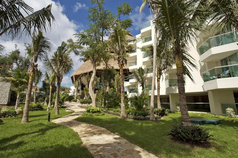 Resort grounds with palm trees, stone path and palapa structure at Grand Park Royal Cozumel
