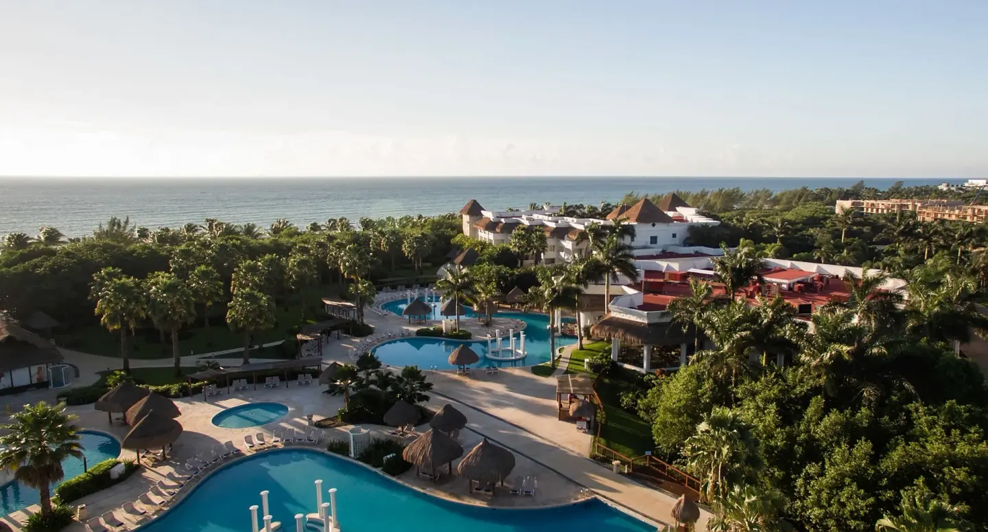 An aerial view shows pools, palms, resort buildings, and the sea at Grand Riviera Princess.
