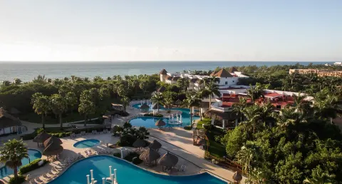 An aerial view shows pools, palms, resort buildings, and the sea at Grand Riviera Princess.