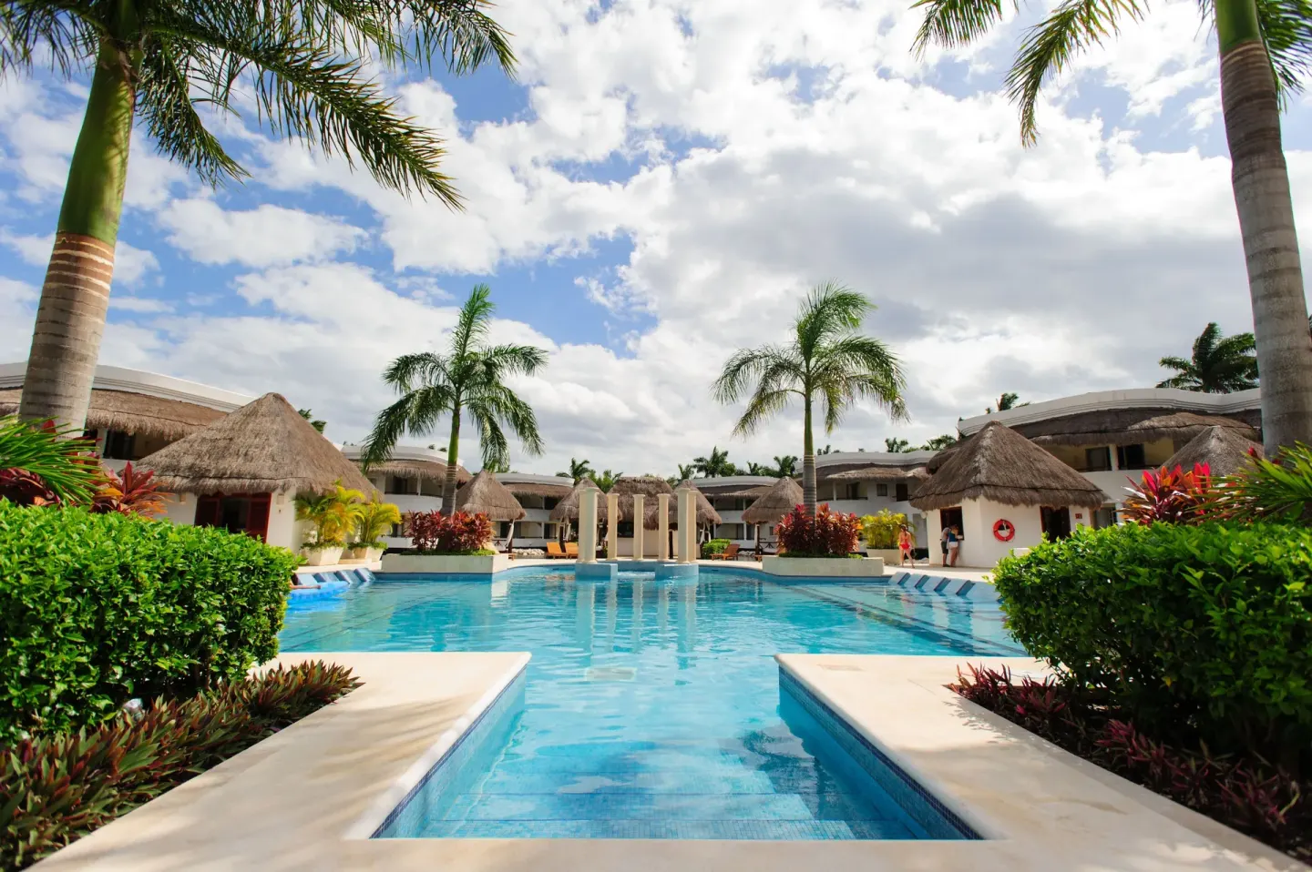 Palm-lined resort pool with thatched roofs at Grand Riviera Princess.