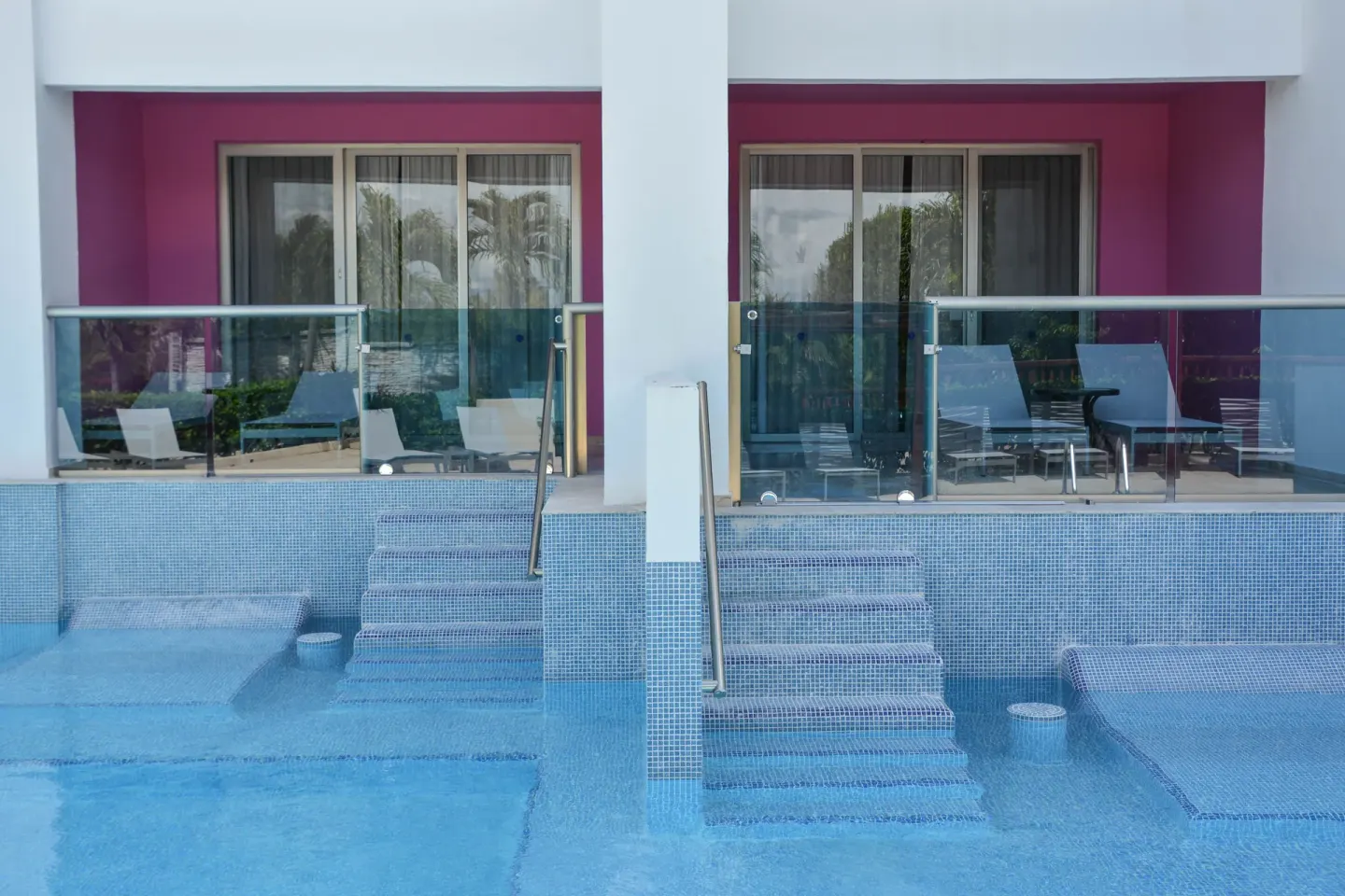Swim-up room terraces with glass railings and pool steps at Grand Riviera Princess.