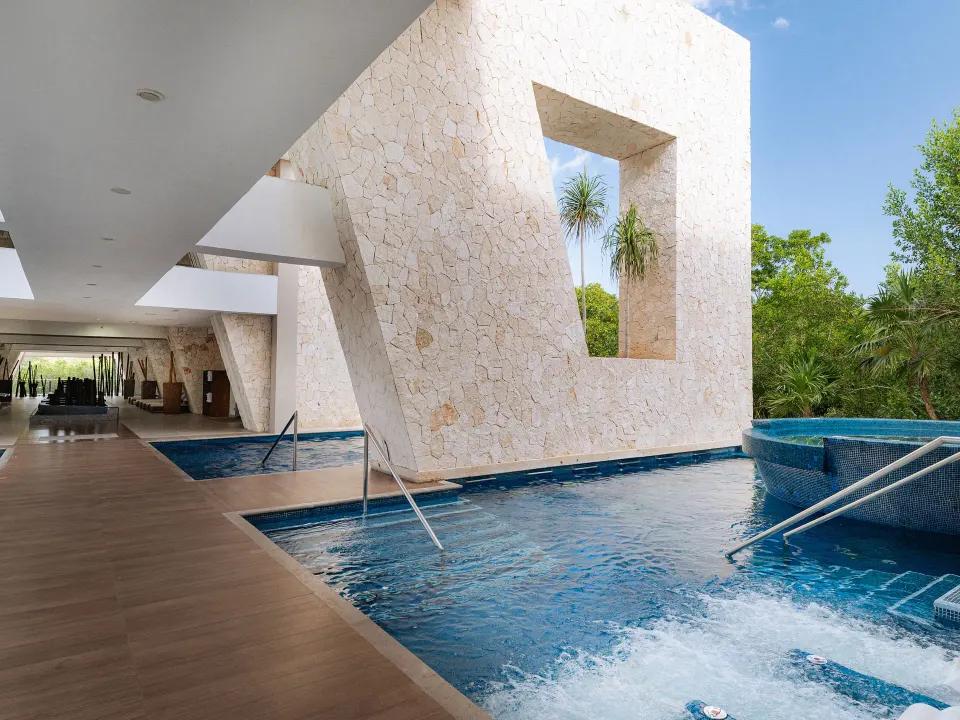 Indoor-outdoor pool area with stone architectural wall and water features at Grand Sirenis Riviera Maya Resort & Spa