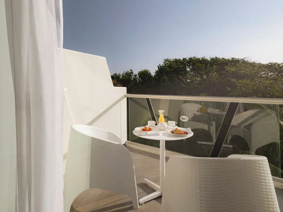 Private balcony with table set for breakfast and woven chairs at Grand Sirenis Riviera Maya Resort & Spa
