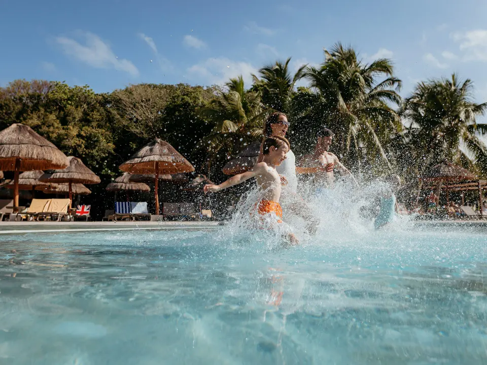 Children running and splashing in the resort pool near palapas at Grand Sirenis Riviera Maya Resort & Spa