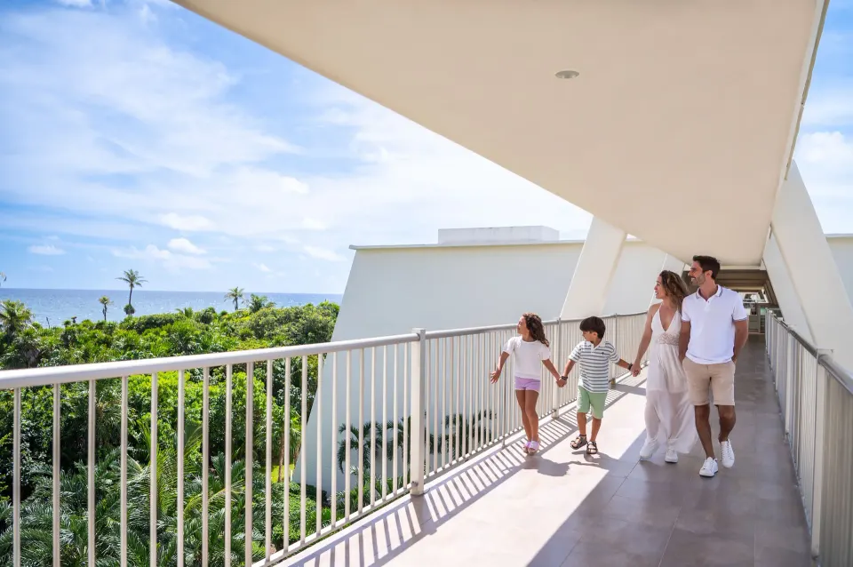 Family walking along an outside hotel corridor with ocean view at Grand Sirenis Riviera Maya Resort & Spa