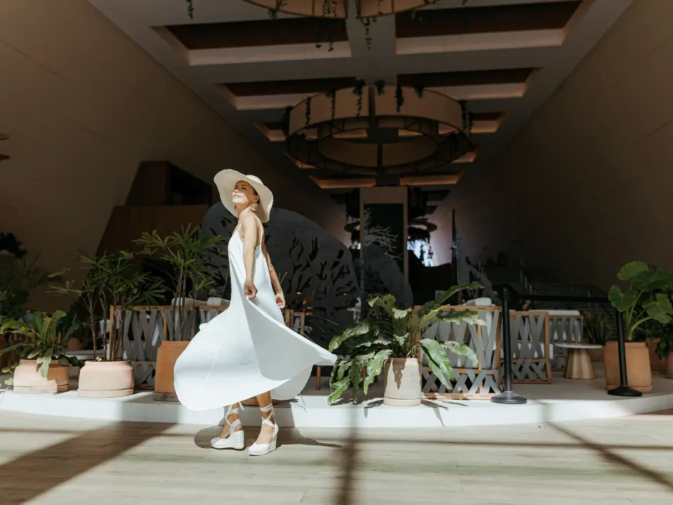 Woman in white dress walking through the sunlit lobby at Grand Sirenis Riviera Maya Resort & Spa
