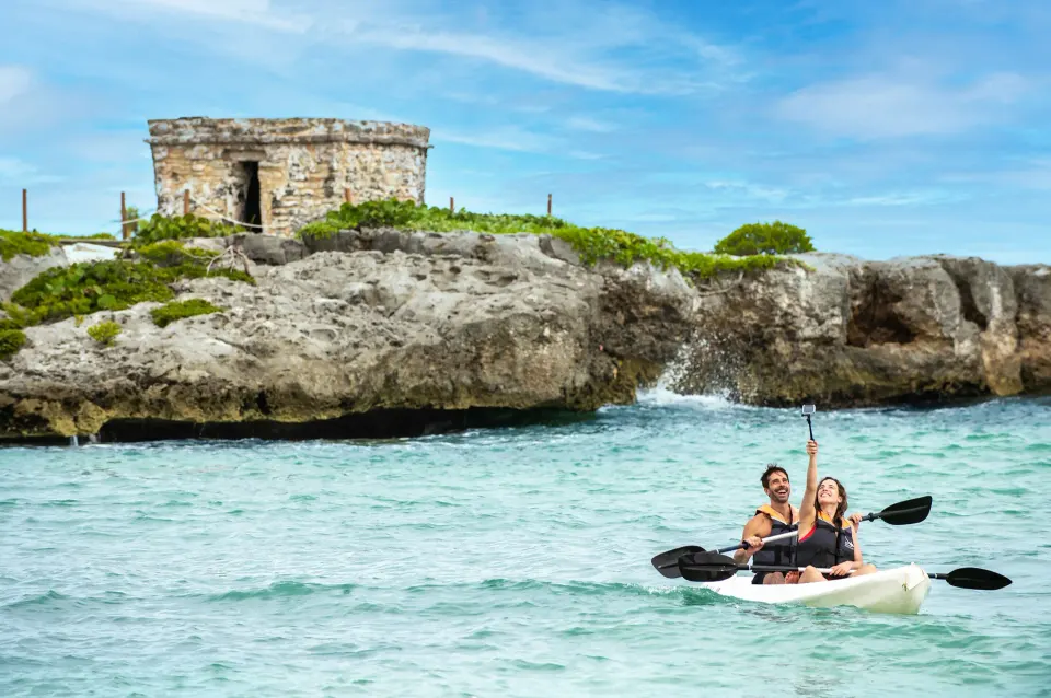 Two guests kayaking near a rocky shoreline with a small stone ruin at Grand Sirenis Riviera Maya Resort & Spa