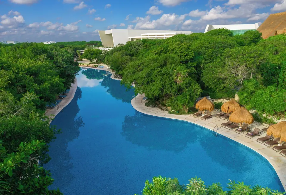 Long winding pool flanked by trees and palapas at Grand Sirenis Riviera Maya Resort & Spa