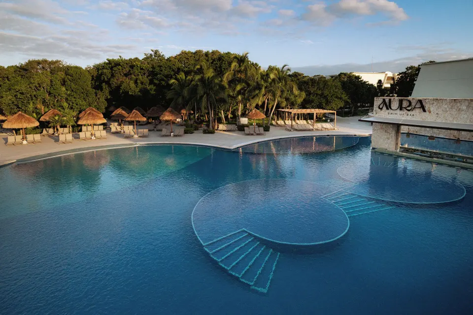 Large resort pool with palapas and the Aura building at Grand Sirenis Riviera Maya Resort & Spa