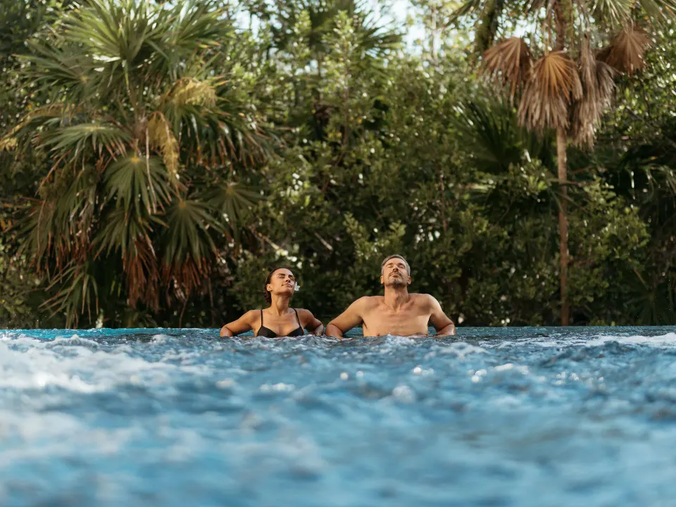Couple relaxing in an outdoor pool with tropical trees at Grand Sirenis Riviera Maya Resort & Spa