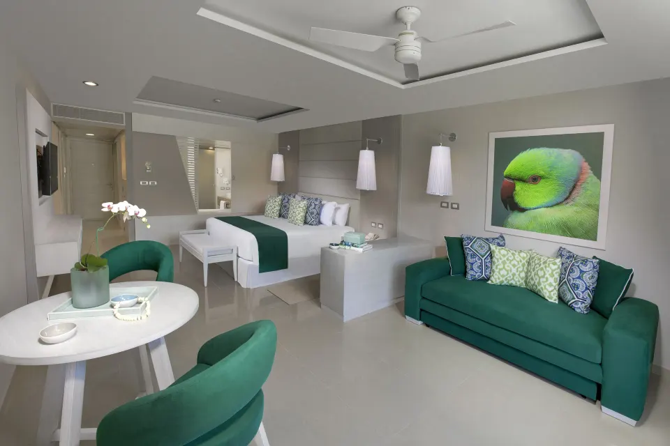 Spacious suite with king bed, green sofa and bird artwork at Grand Sirenis Riviera Maya Resort & Spa