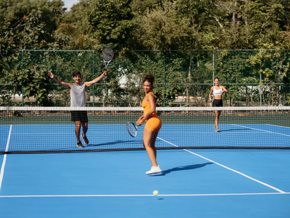 People playing doubles on a blue outdoor tennis court at Grand Sirenis Riviera Maya Resort & Spa