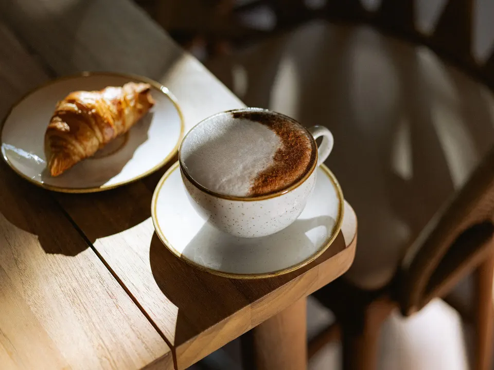Cup of cappuccino and croissant on a wooden table at Grand Sirenis Riviera Maya Resort & Spa
