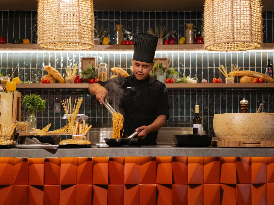Chef tossing spaghetti at a demonstration counter with baskets of pasta at Grand Sirenis Riviera Maya Resort & Spa